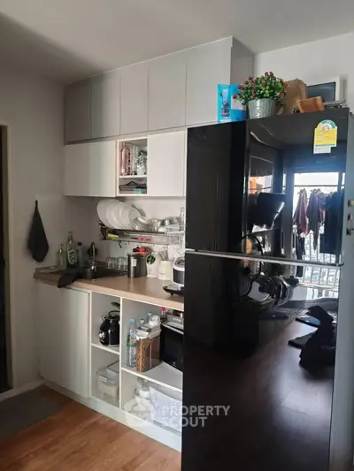 Modern kitchen with sleek cabinetry and appliances, featuring a glossy black refrigerator and open shelving.