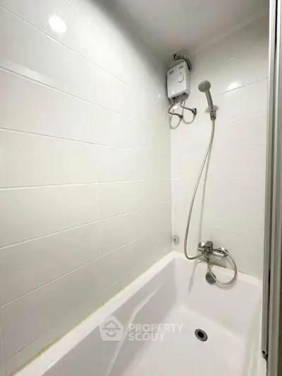 Modern bathroom with white tiles and bathtub featuring a showerhead and water heater.