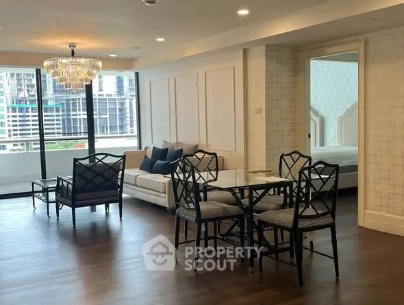 Spacious living room with elegant chandelier and modern furniture, featuring large windows with city view.