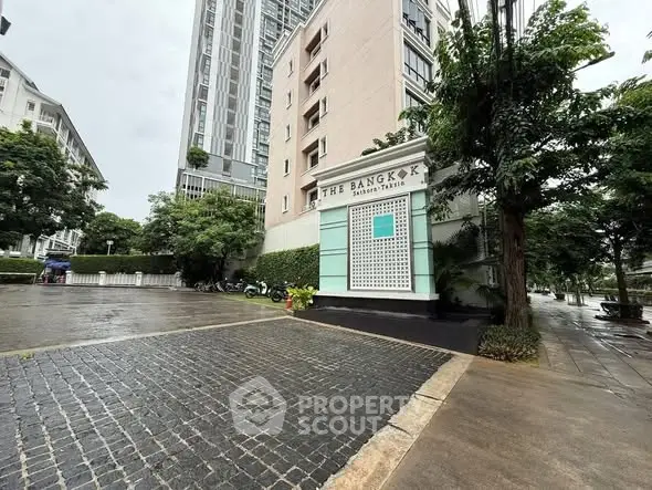 Modern building entrance with lush greenery and paved walkway in urban setting.