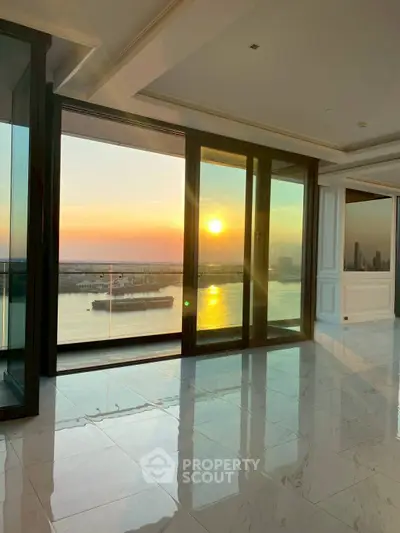 Luxurious waterfront living room with stunning sunset view through large glass doors.