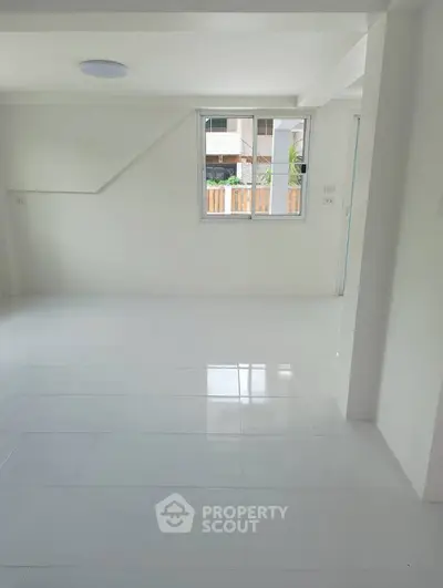 Spacious and bright interior with large window and white tiled flooring, perfect for modern living.