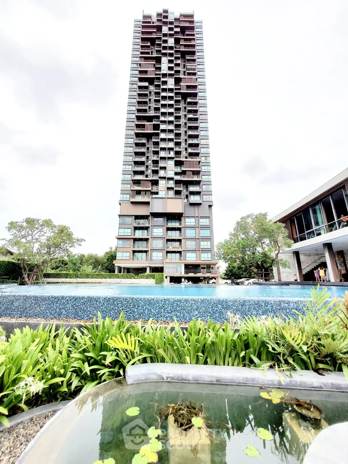 Stunning high-rise building with lush garden and inviting pool in modern urban setting.
