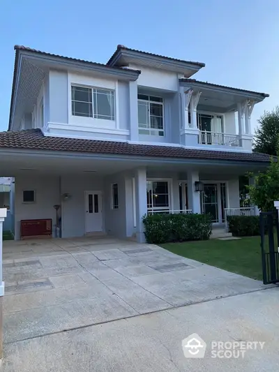 Elegant two-story house with spacious driveway and lush green lawn, featuring a large balcony and covered porch in a serene neighborhood.