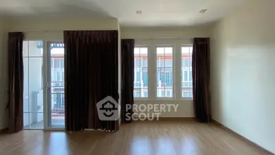 Spacious empty room with large windows and balcony access, featuring elegant dark curtains and wooden flooring.
