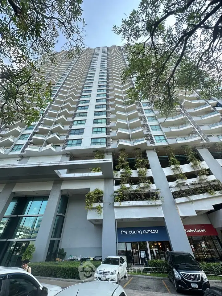Stunning high-rise building exterior with modern design and retail shops at the base, surrounded by lush greenery.