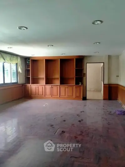 Spacious living room with built-in wooden shelves and large window for natural light.