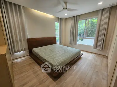 Spacious bedroom with large window and modern wooden bed frame, offering serene garden views.