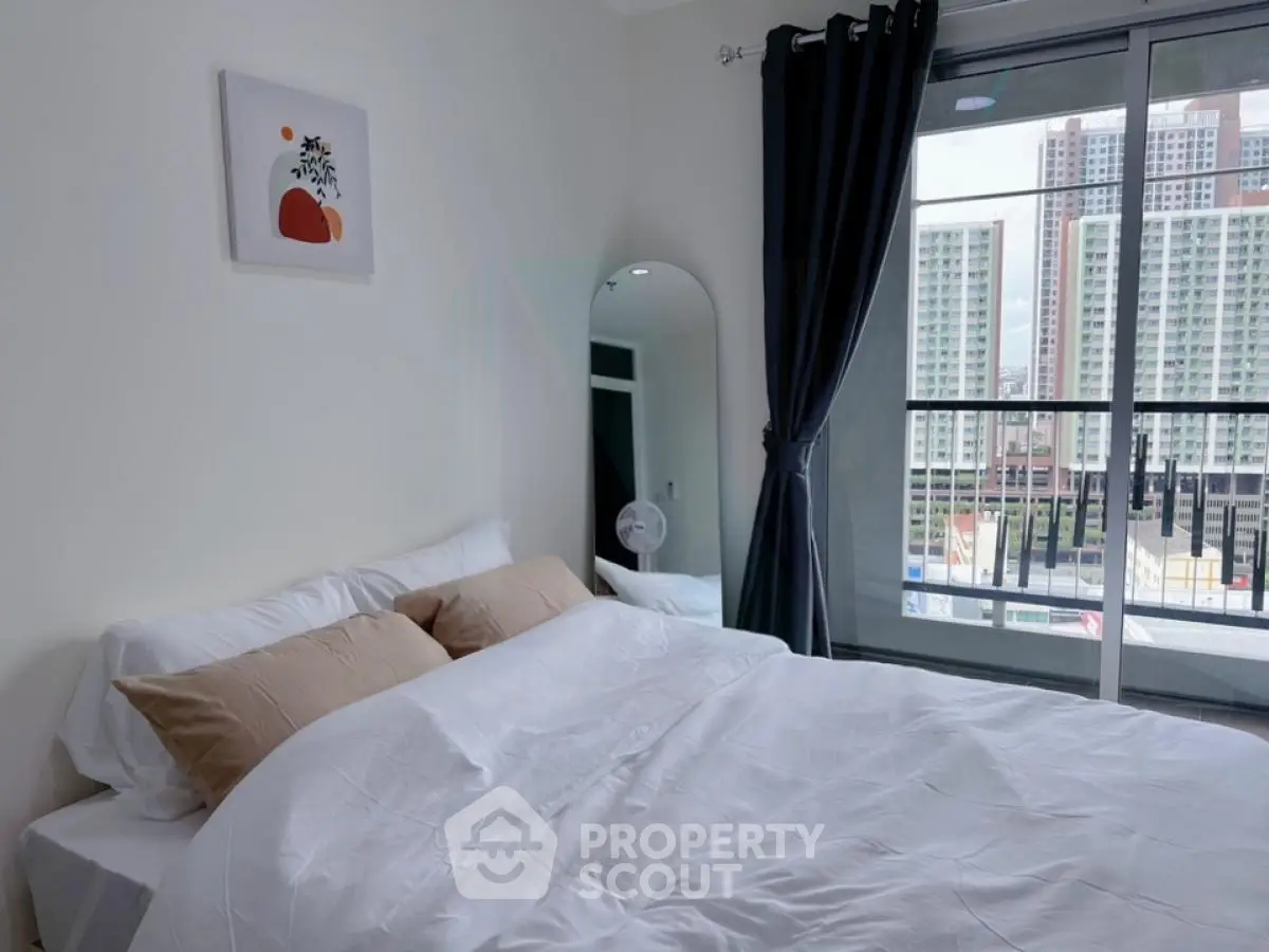 Modern bedroom with large window and city view, featuring stylish decor and cozy bedding.