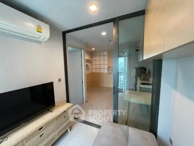 Modern apartment interior with sliding glass doors and wooden furniture, featuring a compact living area and air conditioning.