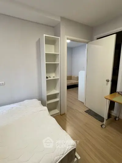 Cozy bedroom with minimalist design and wooden flooring, featuring a white bed and open shelving.