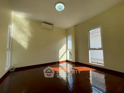 Spacious sunlit room with polished wooden floors and large windows, perfect for a cozy living space.