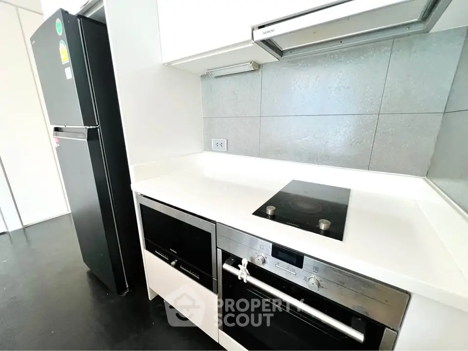 Modern kitchen with sleek appliances and minimalist design, featuring a built-in oven and electric cooktop.