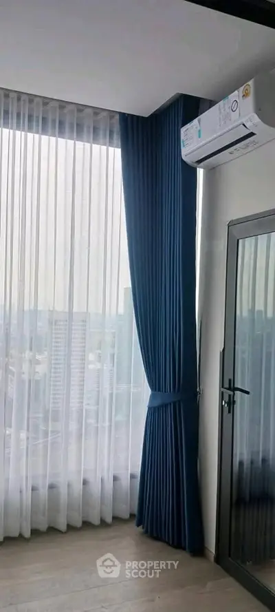 Modern high-rise apartment with floor-to-ceiling windows and city view, featuring elegant blue curtains and air conditioning.