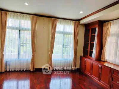 Spacious living room with elegant wooden flooring and large windows with curtains.