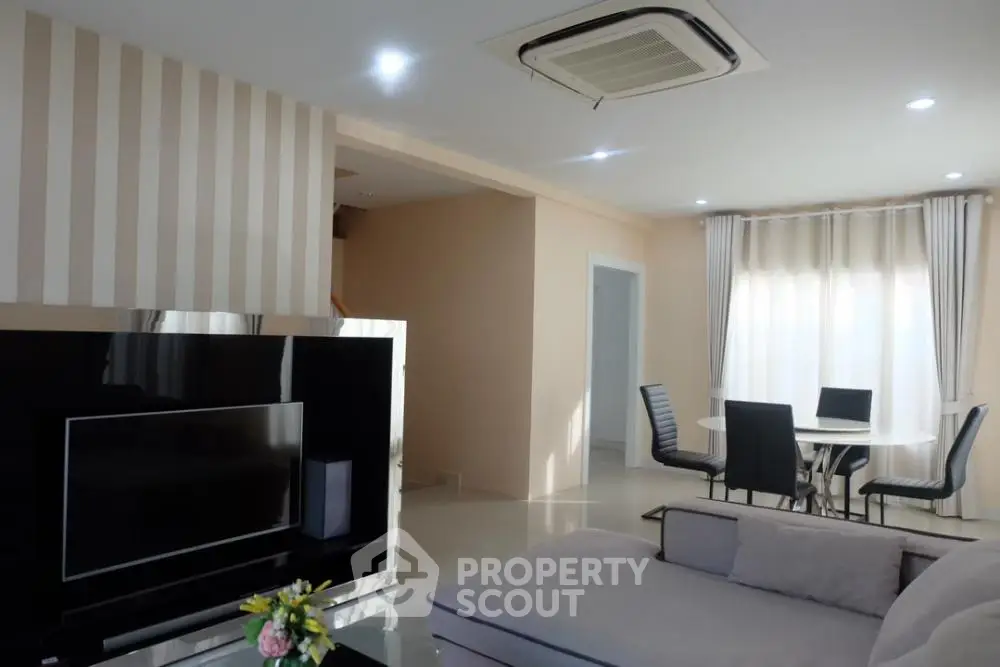 Spacious and well-lit living room with modern furnishings, large TV, and elegant dining area, perfect for entertaining and relaxation.