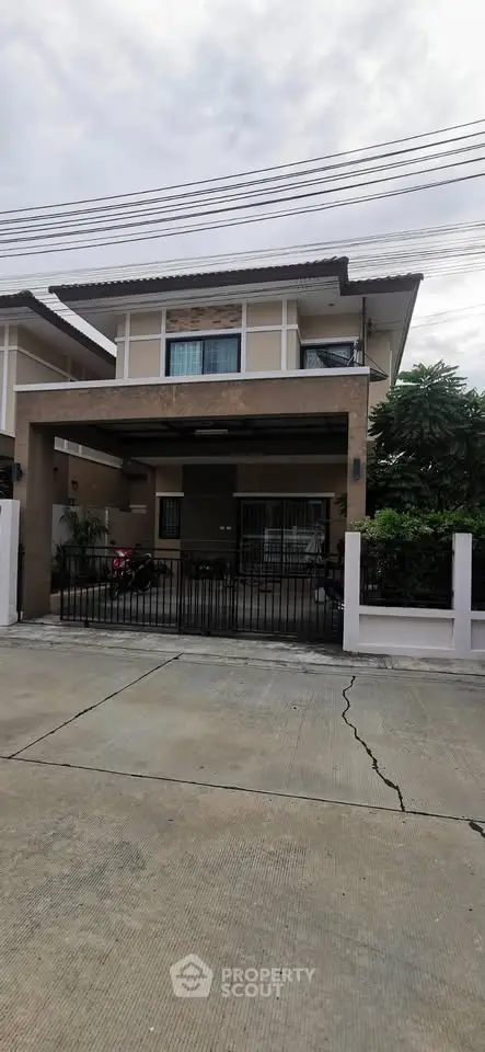 Modern two-story house with gated driveway and lush greenery in suburban neighborhood.