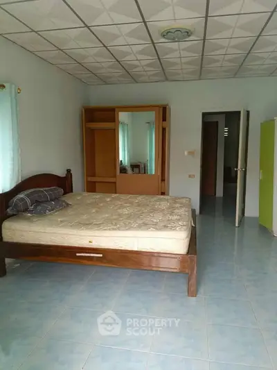 Spacious bedroom with wooden bed and wardrobe, tiled floor, and natural light.