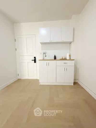 Minimalist kitchen with white cabinets and light wood flooring