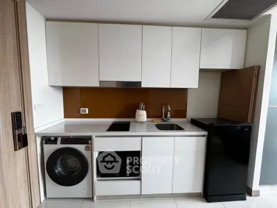 Modern kitchen with sleek white cabinets, washing machine, and compact fridge