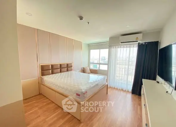 Spacious bedroom with large window and modern furnishings in a bright apartment.