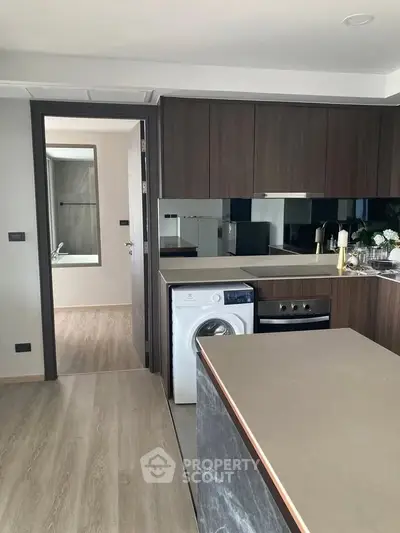 Modern kitchen with sleek cabinetry and built-in appliances, featuring a washing machine and open layout.