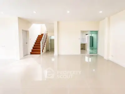 Spacious open-plan living area with glossy tiled floors and wooden staircase, perfect for modern living.