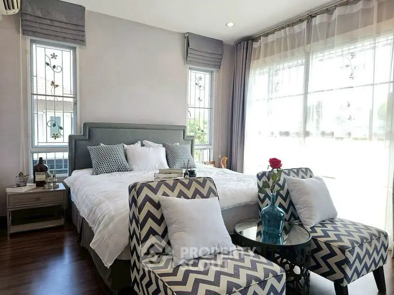 Elegant bedroom with stylish decor and natural light, featuring cozy seating and modern design.