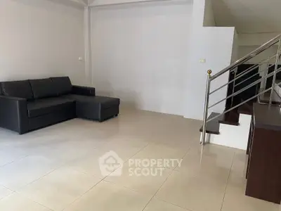 Spacious modern living room with sleek black sofa and elegant staircase