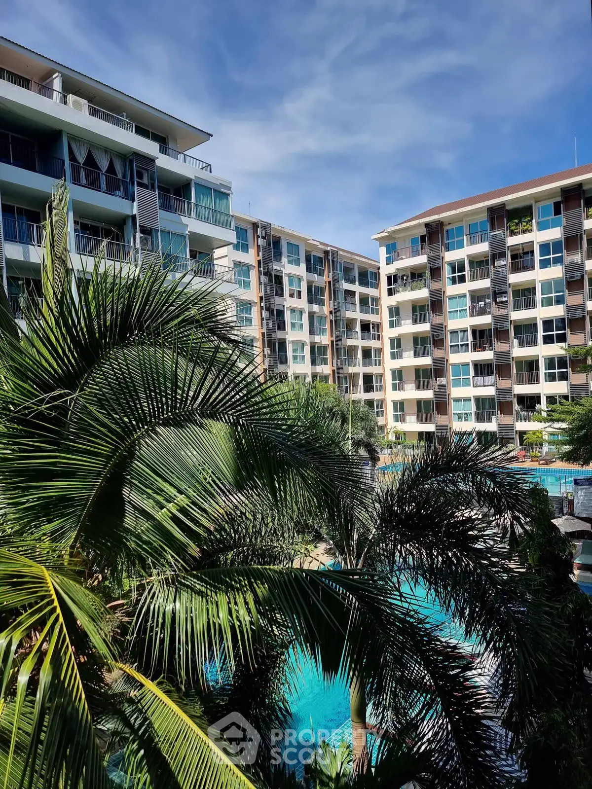 Luxurious condominium complex with lush greenery and inviting pool area under a clear blue sky.