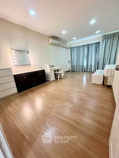 Spacious bedroom with wooden flooring and modern decor, featuring a vanity and ample natural light.