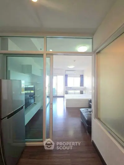 Modern apartment interior with glass partitions, sleek kitchen, and spacious living area leading to a bright bedroom.