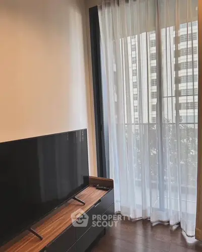 Modern living room with sleek TV stand and floor-to-ceiling windows offering city views.