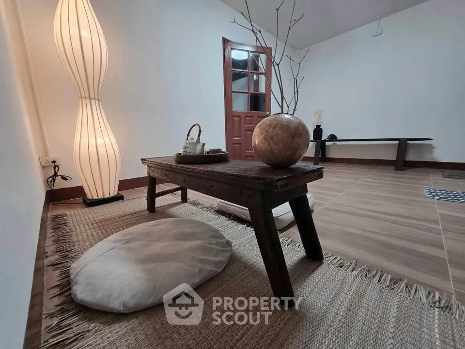 Minimalist living room with wooden table and floor cushion, featuring a unique floor lamp.