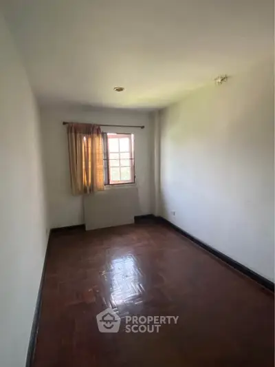 Spacious empty room with wooden flooring and natural light from window.