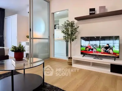 Modern living room with sleek TV setup and stylish decor, featuring a glass coffee table and wooden flooring.