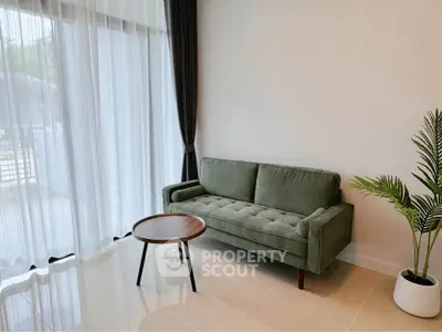 Modern living room with green sofa and round wooden table near large window.