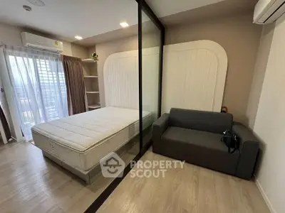 Modern bedroom with glass partition, cozy sofa, and natural light from large window.