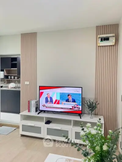 Modern living room with sleek TV stand and stylish decor, open kitchen layout visible in background.