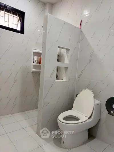 Modern bathroom with sleek white tiles and open shelving, featuring a contemporary toilet design.