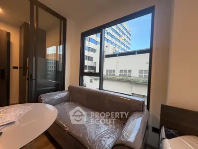 Modern living room with large window and city view, featuring a sleek sofa and stylish decor.