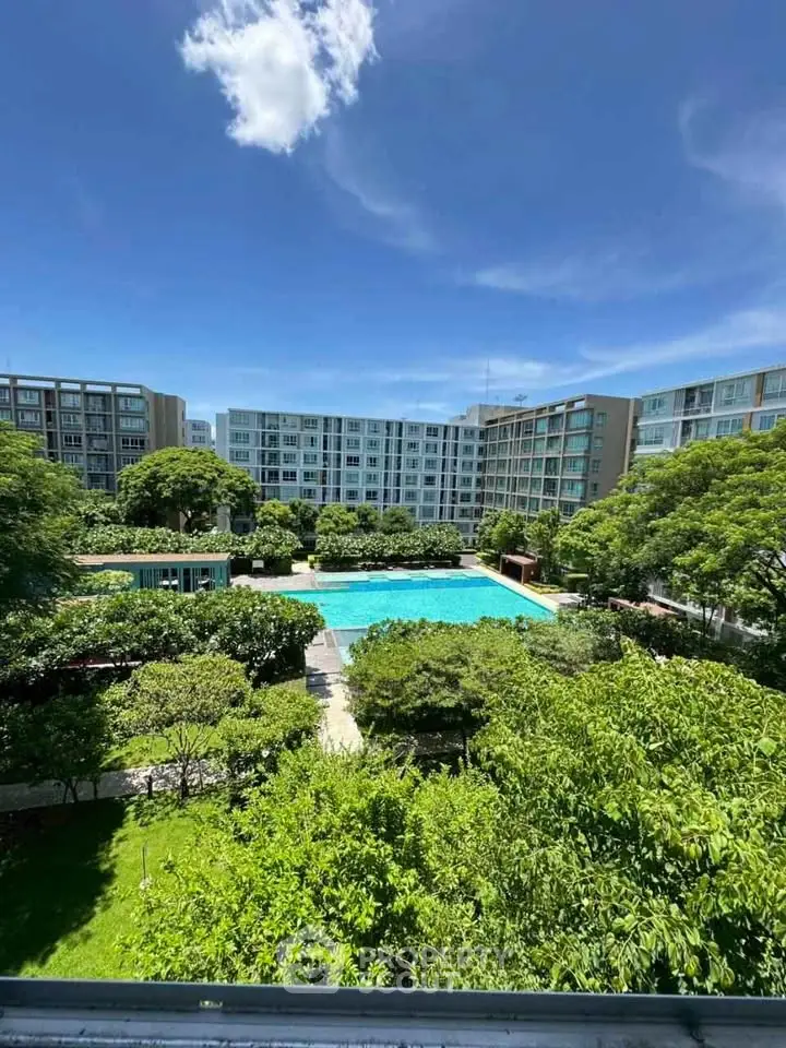 Stunning view of modern apartment complex with lush gardens and inviting pool under clear blue sky.