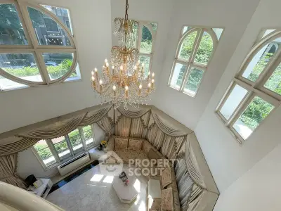 Luxurious living room with high ceiling, elegant chandelier, and large windows offering scenic views.