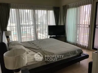 Spacious bedroom with large windows offering a stunning city view, modern decor, and natural light.