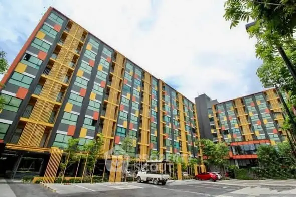 Modern colorful apartment building with spacious parking area and lush greenery.
