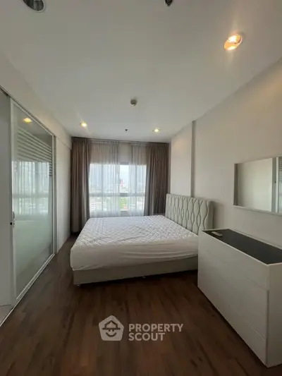Spacious bedroom with large window and modern furnishings in a stylish apartment.