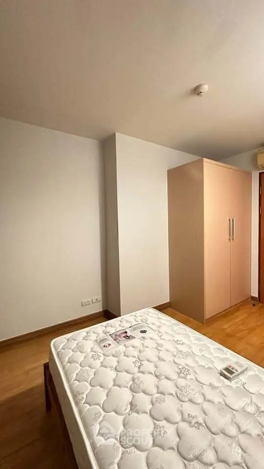Spacious bedroom with wooden flooring and ample natural light, featuring a wardrobe and a comfortable bed.