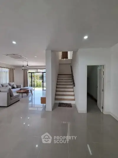 Spacious modern living room with staircase and large windows offering natural light.