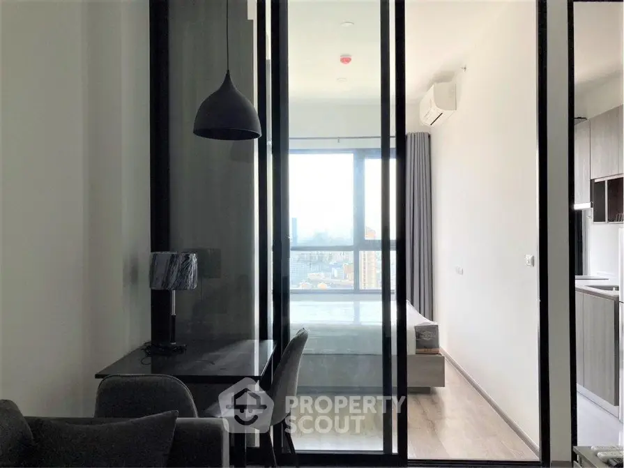Modern apartment interior with glass partition, featuring a cozy living area and a bright bedroom with city view.