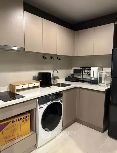 Modern kitchen with sleek beige cabinetry and built-in appliances, including a microwave, oven, and washing machine, offering a functional and stylish cooking space.